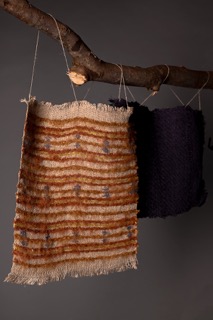 An Image of two upholstery samples hung on a branch. The samples are made from homegrown and hand-spun linen, and dyed with natural dyes.