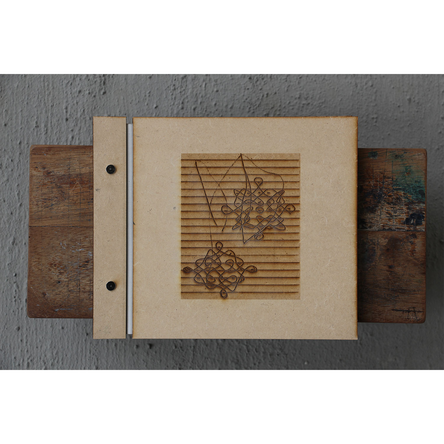 Laser-cut MDF hardcover book resting on a teak wooden stool, featuring embossed prints and metal binding screws