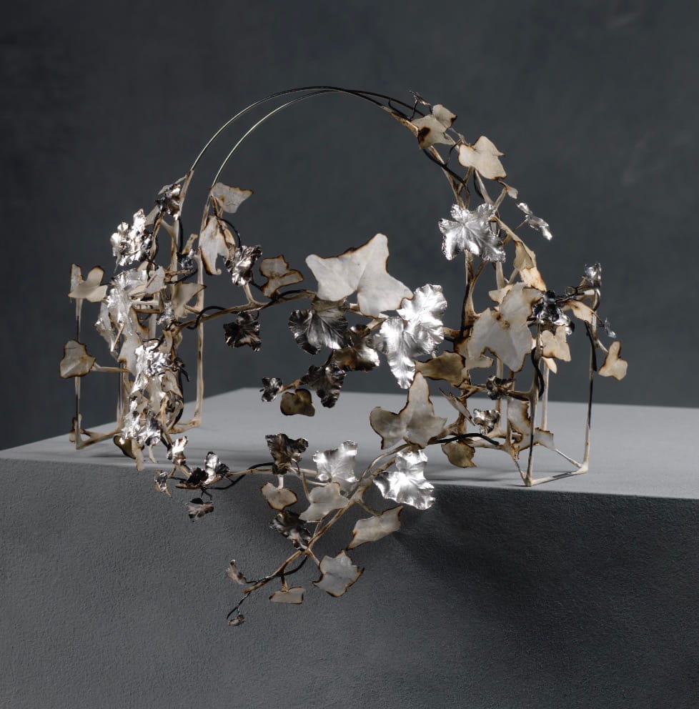 A contemporary wearable headpiece exploring the contrast between structured silver forms and organic paper mâché surfaces.