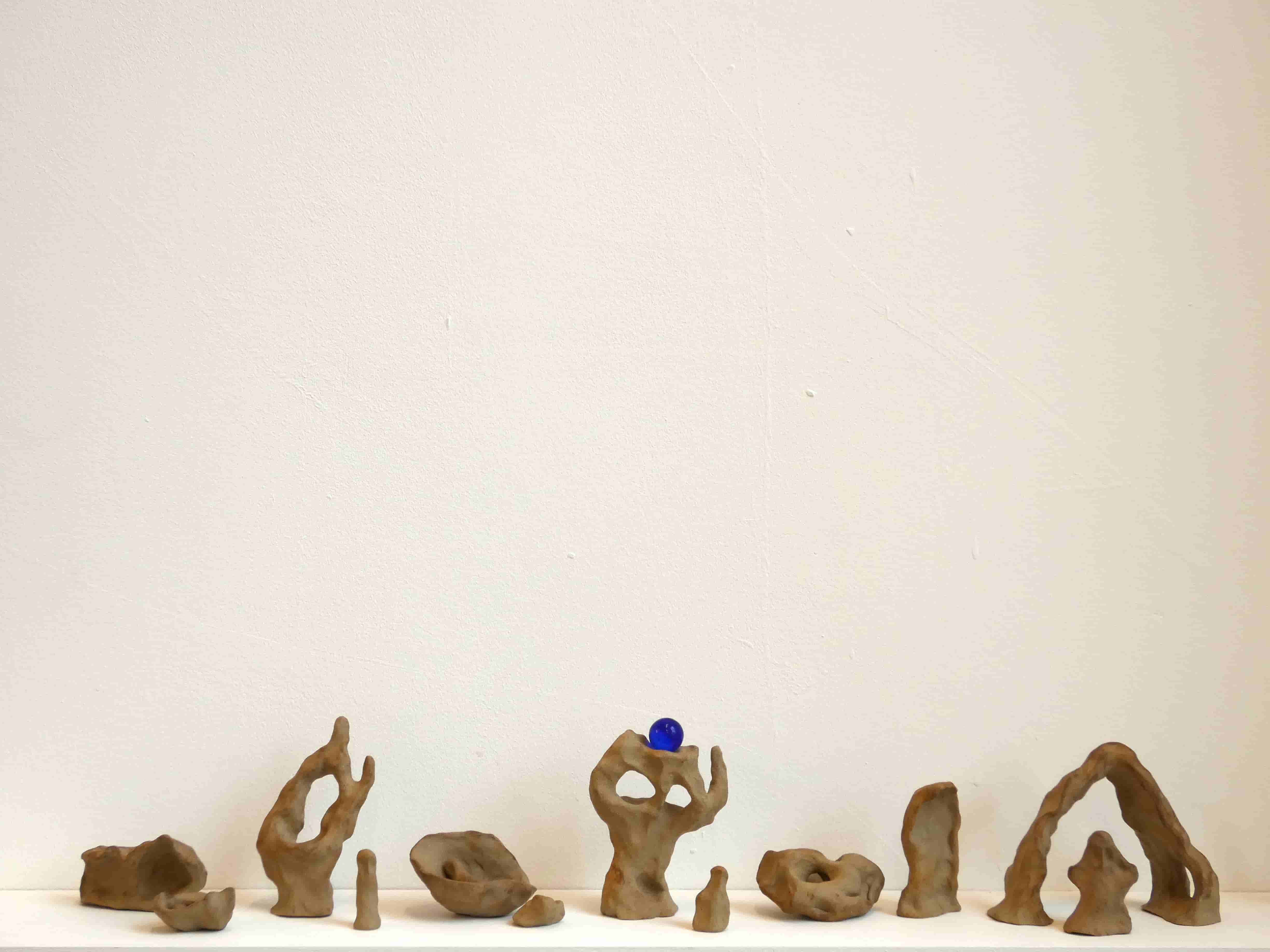 Abstract ceramic sculptures and a blue marble on a white shelf and white wall 