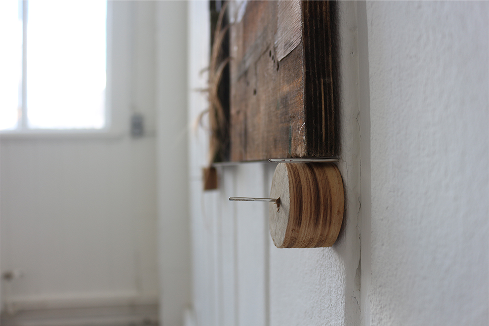 Image of wooden sculpture installed onto wall using sewing needles, with hair binding.