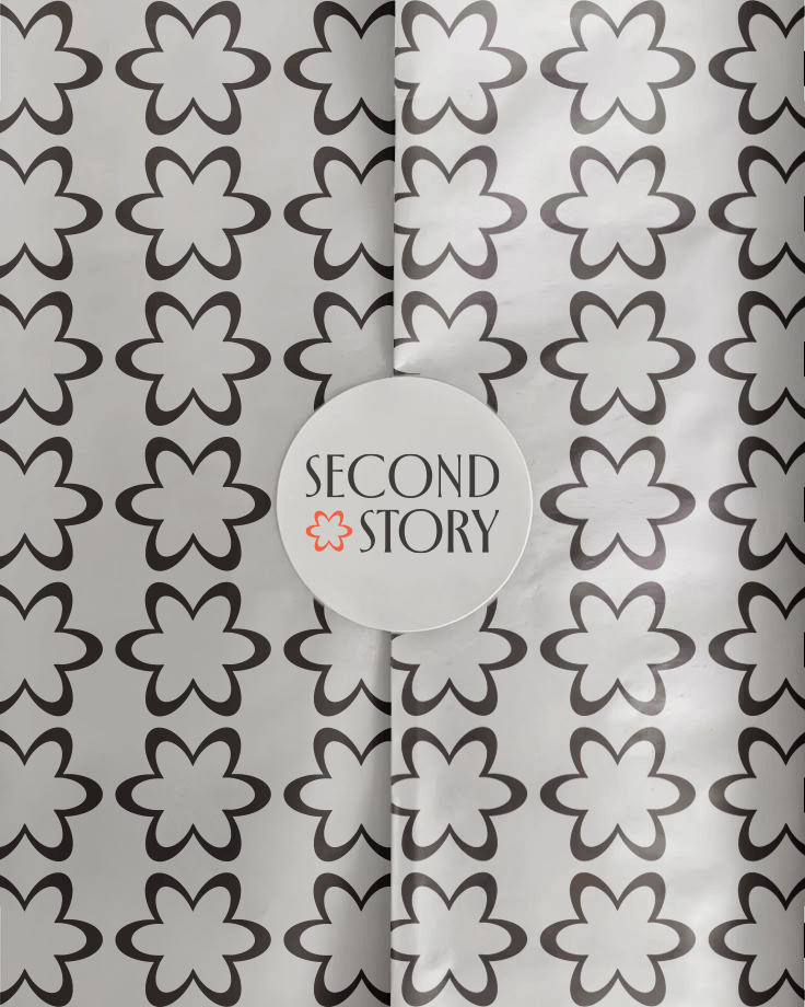     Close up of Second Story branded wrapping paper with a repeating black flower pattern and a round white sticker showing the Second Story logo.