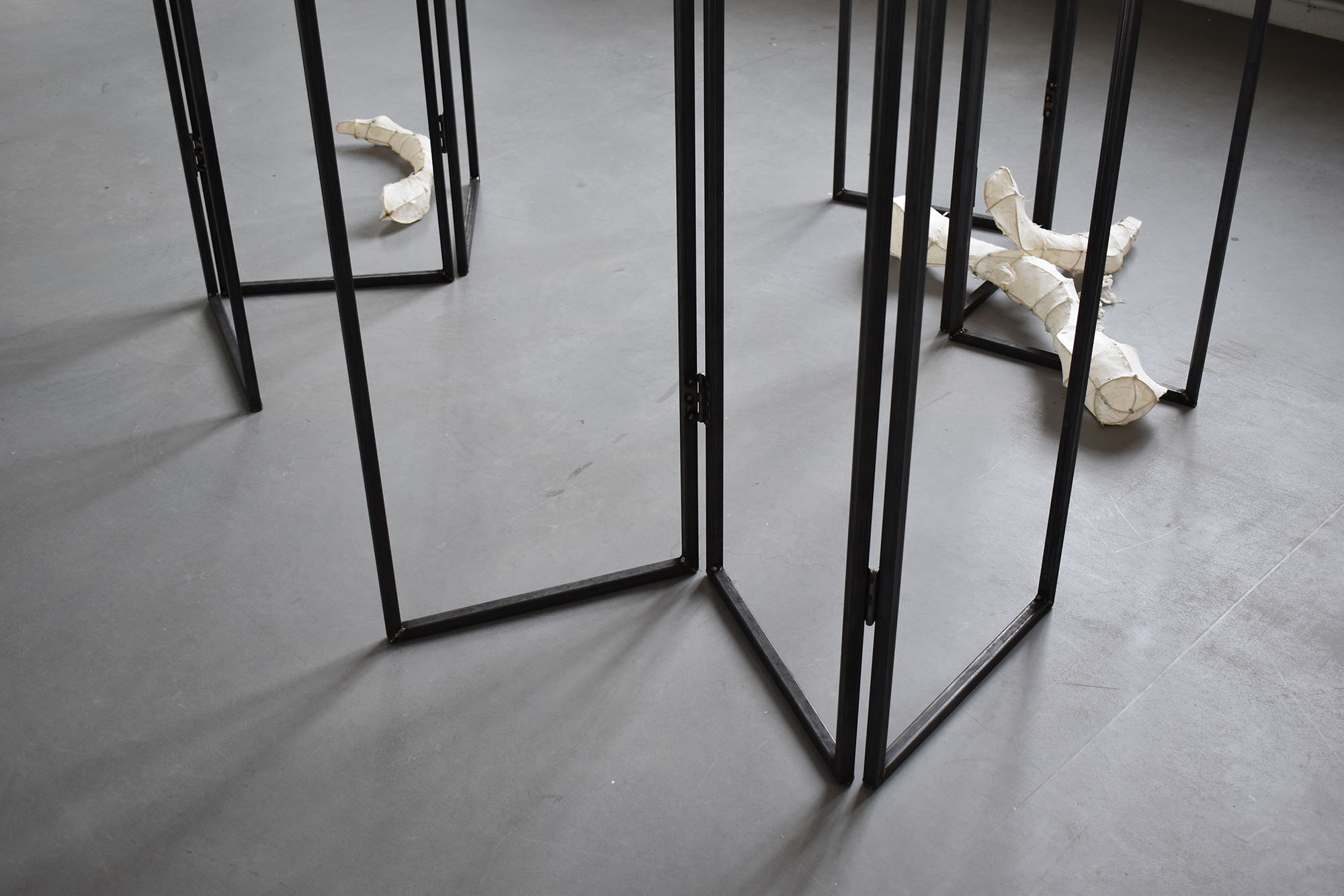 A close-up shot of the bottom edges of three hollow metal dressing screens. A few rice paper sculptures are scattered amongst them.A close-up shot of the bottom edges of three hollow metal dressing screens. A few rice paper sculptures are scattered amongst them.