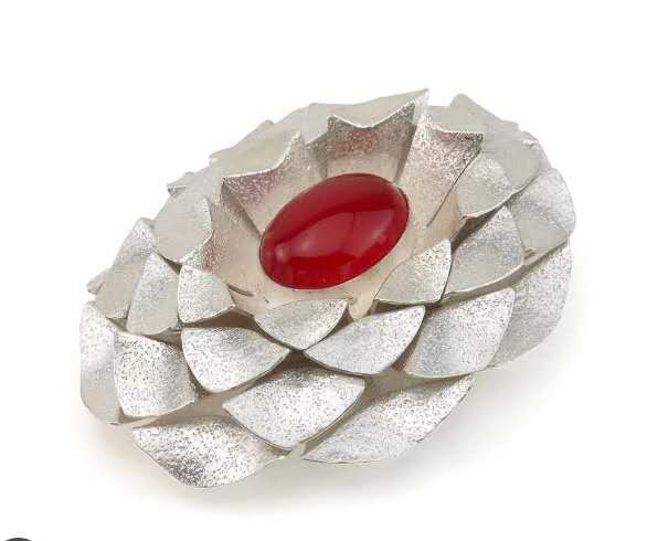 Oval layered brooch made of folded silver metal with gold elements arranged in a pinecone-like structure, centred with a polished  carnelian stone and featuring overlapping geometric forms inspired by natural growth patterns.