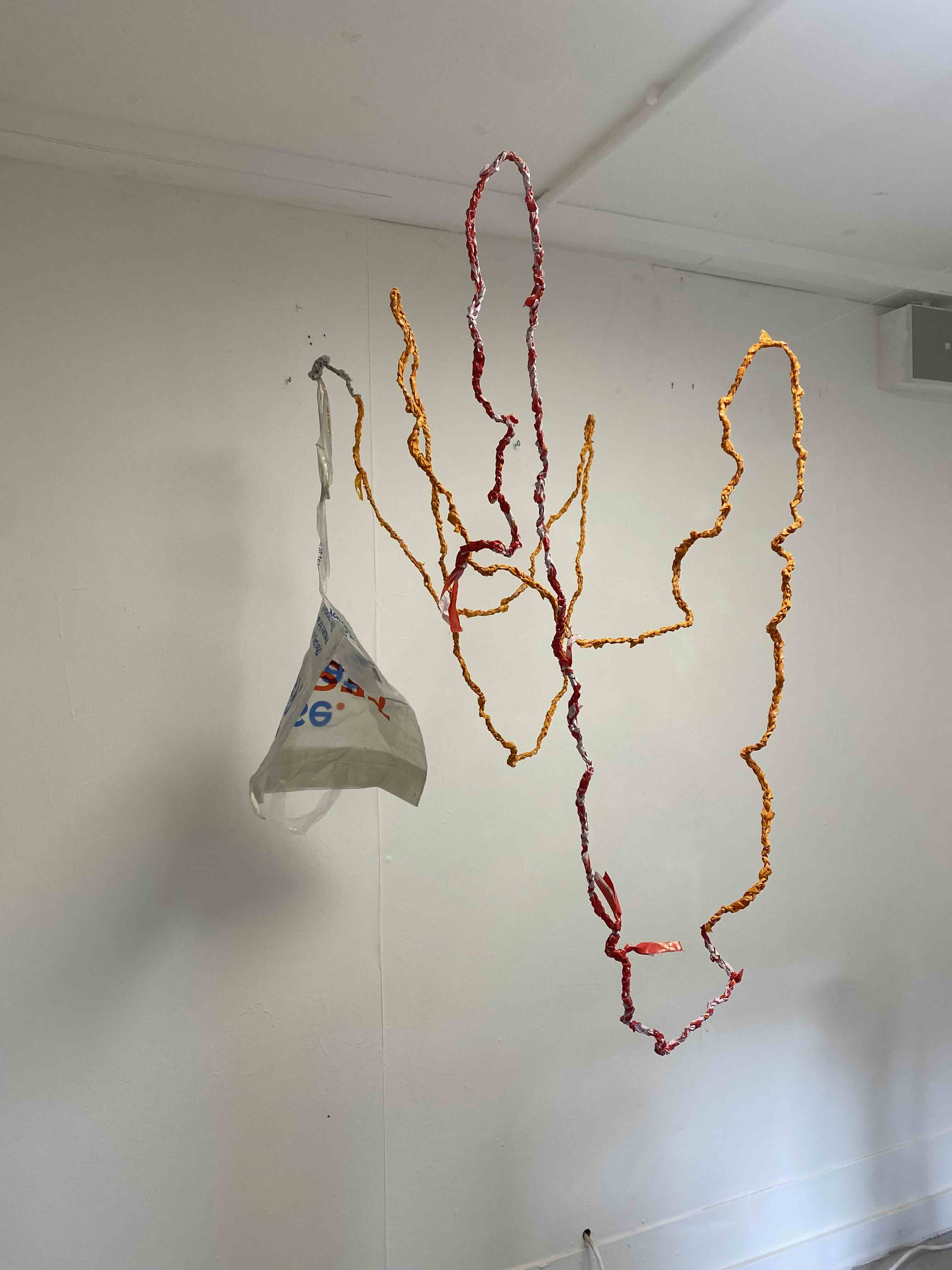 Crochet plastic bags hung over fishing line in a white cube space