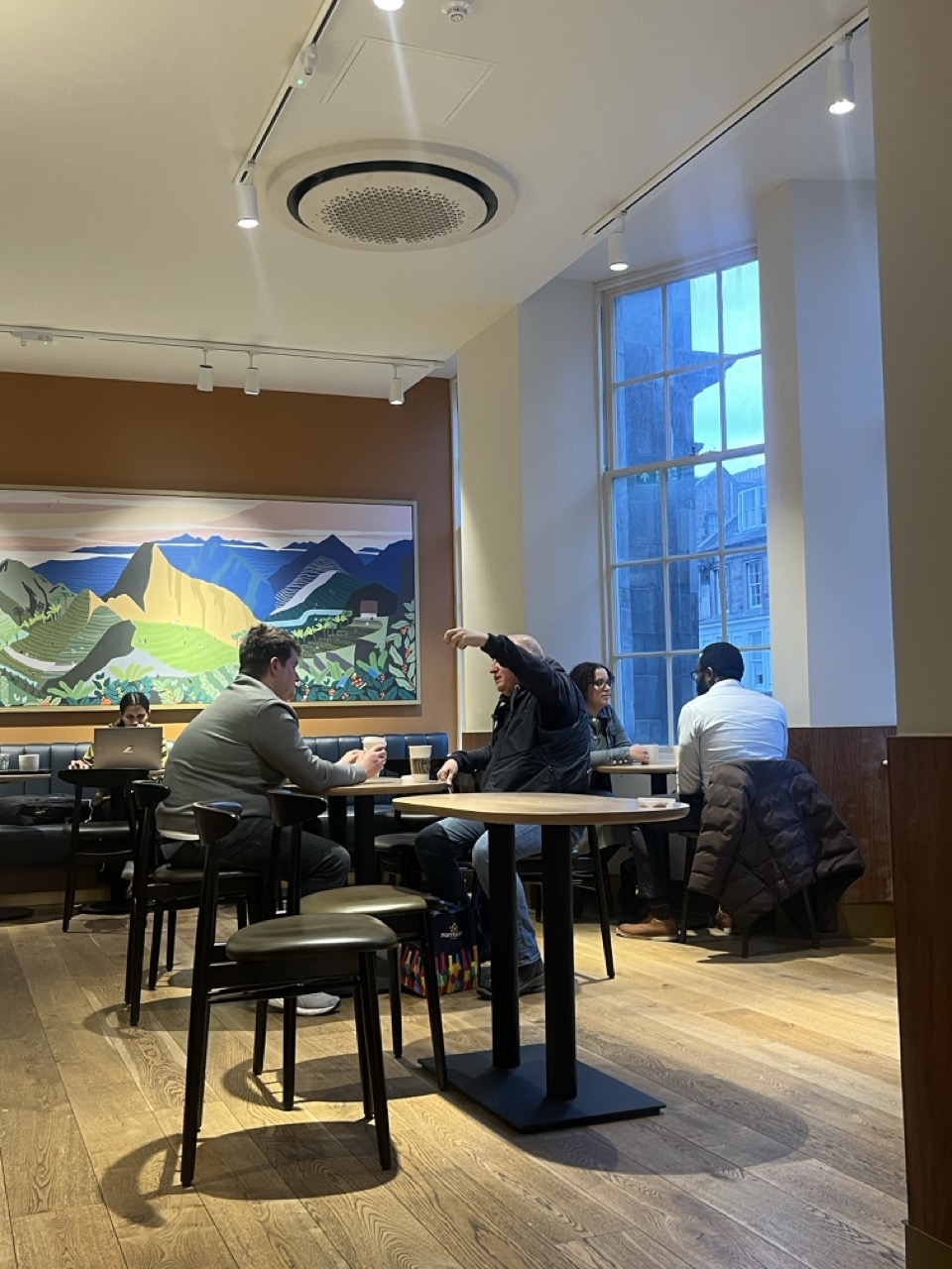 A photograph of the existing café interior shows a neutral open-plan seating arrangement with timber flooring, white walls, track lighting, and large vertical windows bringing natural light into the space.