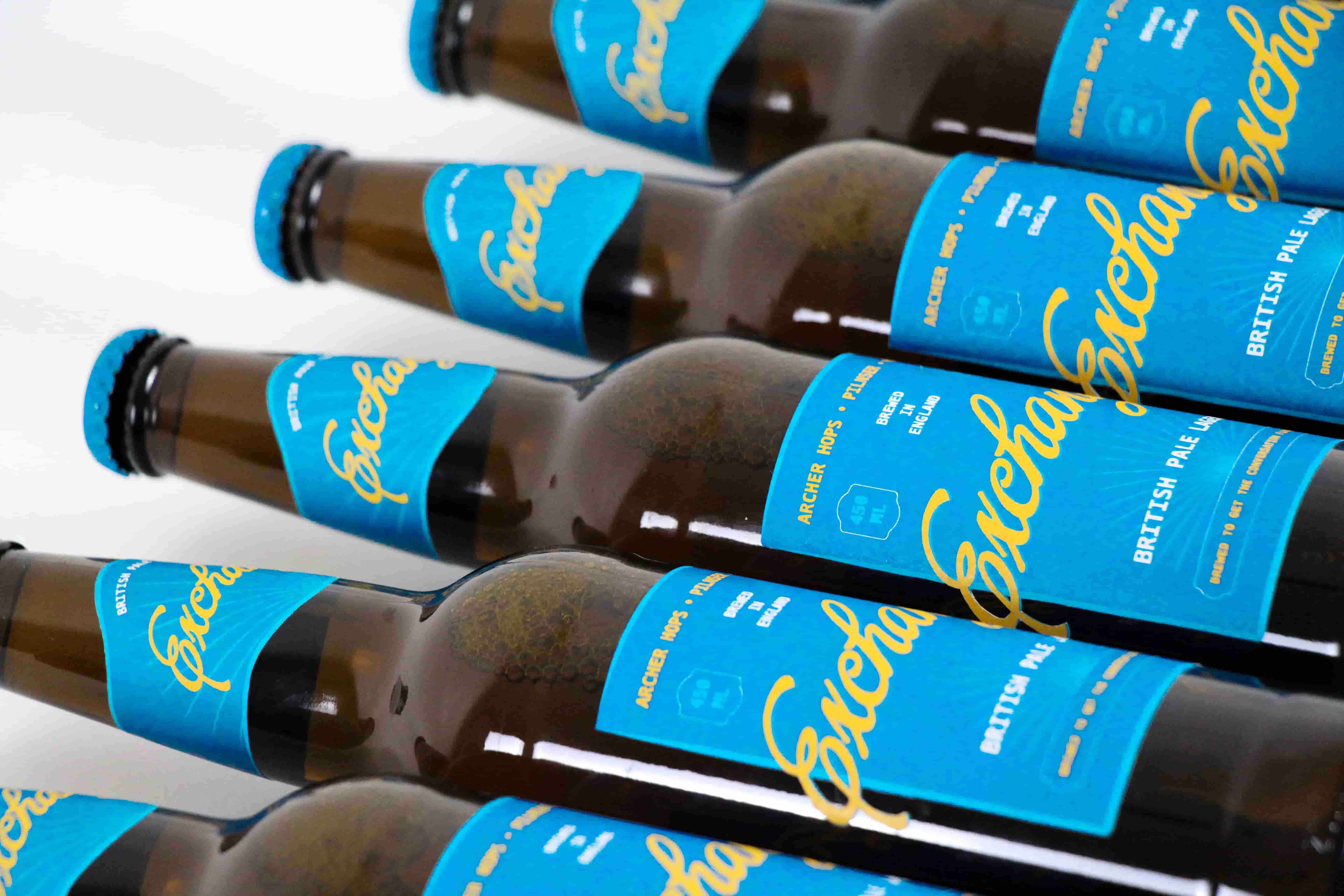     Close up of several ‘Exchange’ beer bottles laid diagonally, showing the teal labels and yellow script logo.