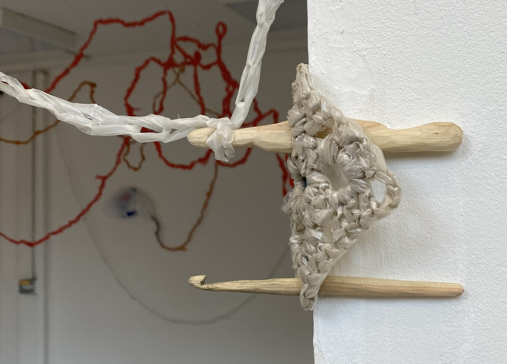Two wooden carved crochet hooks holding a hanging granny square made using plastic bags 