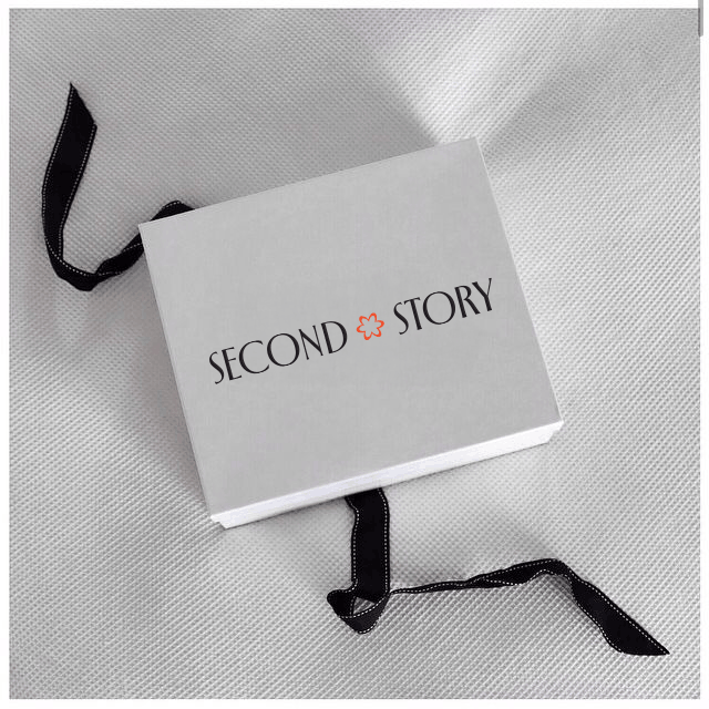     White Second Story gift box on textured fabric, tied with black ribbon and printed with the brand logo.