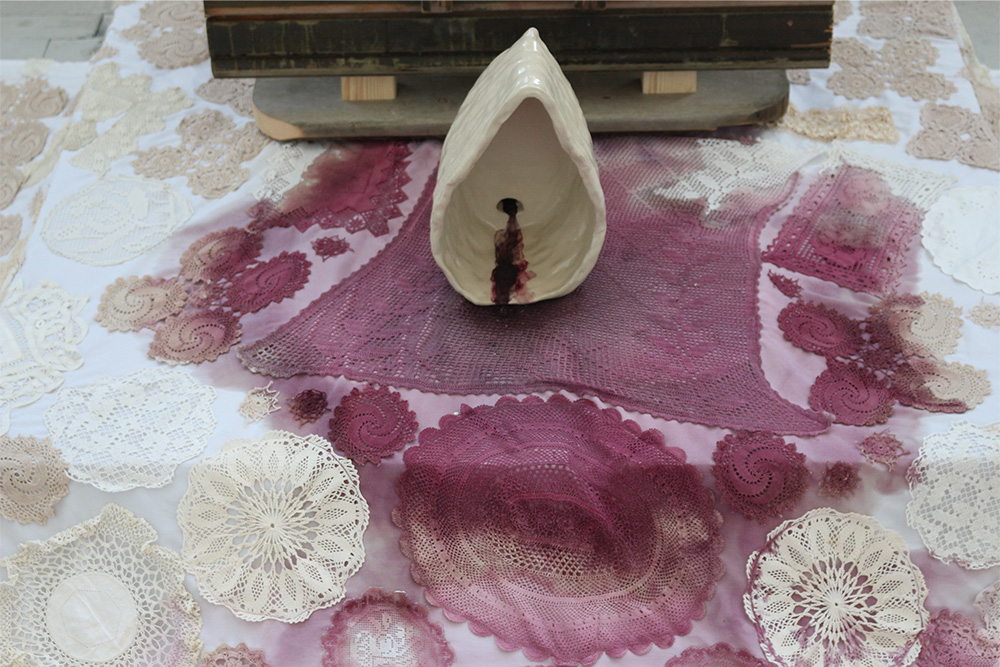 Image of crochet rug stained with red wine and ceramic sculpture.