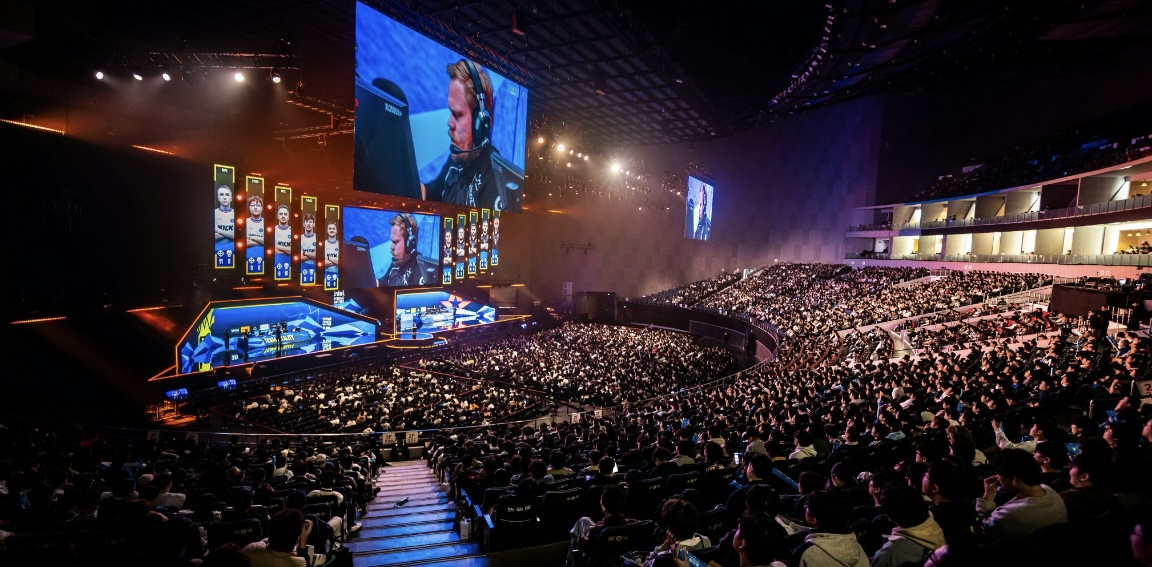 A panoramic view of a large esports arena with a packed audience, illuminated stage, and giant LED screens during a Counter-Strike tournament.